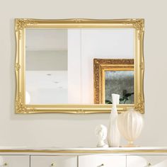 a large gold framed mirror sitting on top of a white dresser next to a vase