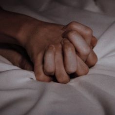 two hands holding each other while laying in bed