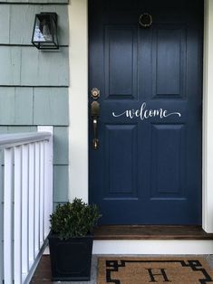 a blue front door with two planters on the steps and a welcome mat in front