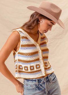 a woman wearing a brown hat standing next to a white wall with her hands on her hips