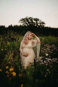 a pregnant woman standing in the middle of a field with her veil over her head