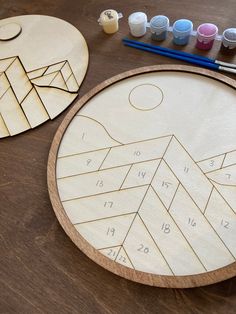 two wooden coasters sitting on top of a table next to paintbrushes and markers