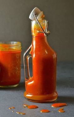 an orange sauce in a glass bottle next to a jar filled with mustard and salt