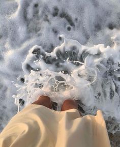 someone is standing in the water with their feet covered by foamy water and sand