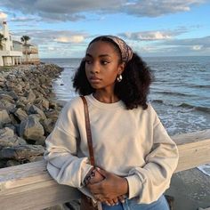 a woman leaning on a wooden fence near the ocean with her hands in her pockets