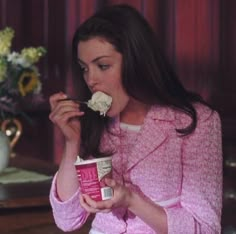 a woman eating food from a cup in front of a vase with flowers on it