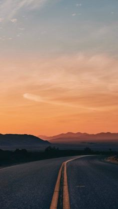 an empty road with mountains in the distance at sunset or dawn, as seen from across the street