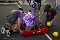 two men working on an electronic device in the middle of a parking lot with yellow balls