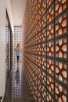 a woman walking down a hallway next to a wall covered in decorative tiles and wooden slats