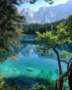 a lake surrounded by mountains and trees with clear water in the foreground, on a sunny day