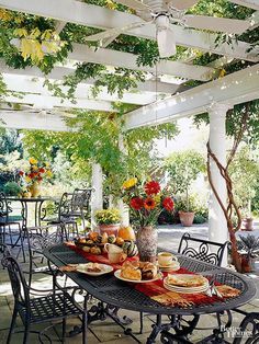 an outdoor dining area with lots of food on the table and chairs, under a pergolated roof