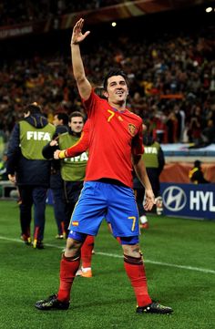 a soccer player waves to the crowd as he walks onto the field with his arms in the air