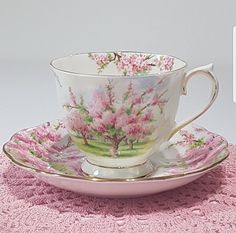 a tea cup and saucer with pink flowers on it sitting on a doily