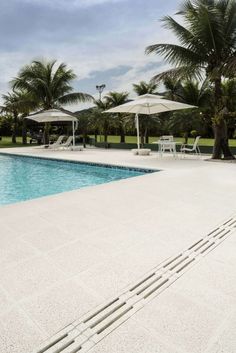 an empty swimming pool surrounded by palm trees and lawn chairs with umbrellas over it