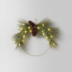 a christmas wreath with pine cones and lights hanging from the side on a white wall