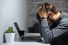 a man sitting at a desk with his head in his hands while using a laptop