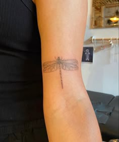 a woman with a tattoo on her arm that has a small dragonfly on it