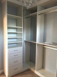 an empty walk - in closet with white shelves and drawers, chandelier hanging from the ceiling