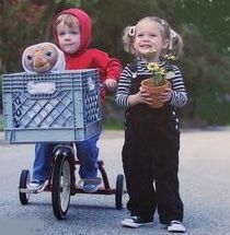 two young children are riding on a bike with stuffed animals in the basket and one is holding a potted plant