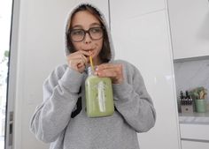 a woman wearing glasses holding a green drink in her hand and looking at the camera