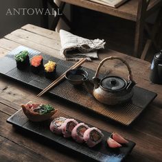 sushi is served on black plates with chopsticks and a teapot in the background