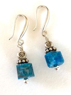 Raw petrol blue apatite earrings with Thai fine silver accents on artisan solid sterling silver ear hooks. Beautiful greenish blue natural apatite faceted gemstone cubes are 9mm and accented with Karen Hill Tribe fine silver triangular beads and sterling silver. Gemstones hang from handmade artisan solid .925 sterling silver ear hooks. Total drop is 1 1/4 inches. Perfect pop of eye catching blue on short artsy ear wires! Turquoise Apatite Gemstone Earrings, Blue Apatite Gemstone Earrings, Handmade Blue Apatite Earrings, Silver Apatite Dangle Earrings, Blue Apatite Earrings For Gift, Blue Apatite Earrings Gift, Blue Earrings For Gift, Turquoise Gemstone Earrings, Aquamarine Earrings