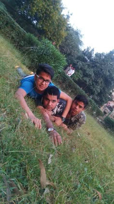 three young men laying on the side of a lush green hillside with trees in the background