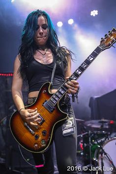 a woman with blue hair playing an electric guitar on stage at a music festival or concert