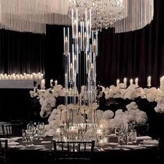 a large chandelier hanging from the ceiling over a table with white flowers and candles