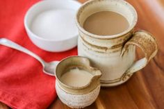 there is a cup of coffee next to a bowl and spoon on the wooden table