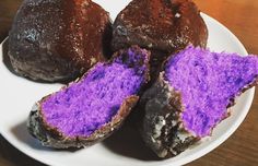 three chocolate muffins with purple frosting on a white plate sitting on a wooden table