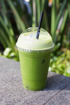 a green smoothie in a plastic cup with a black straw sitting on a table