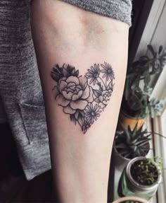 a heart shaped tattoo with flowers and leaves on the side of the arm, next to a potted plant