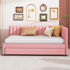 a pink daybed with pillows and pictures on the wall above it in a living room