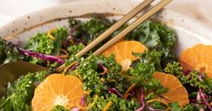 a salad with oranges, onions and greens in a bowl next to chopsticks