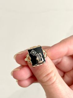 STUNNING bold and regal vintage yellow gold ring with a rectangular black onyx stone in the center and gorgeous scalloped ornate detailing beneath the gold pedestal holding the onyx up. The onyx bears a silver letter "B" on top with a small but mighty diamond stone in the corner. This is an incredible, highly sought-after art deco signet ring. This is estimated to be an antique piece. There is a symbol stamped inside the band beside which I cannot make out. This is presumably the maker's mark but possibly also the gold content. It appears to be a triangle, which apparently has roots in England and may even indicate a higher gold content, such as 14K. Size is approximately 6 - 6.25. Total weight is approximately 2.59 grams. *Note: This listing will ship with TRACKING to ALL destinations, in Luxury Engraved Onyx Ring, Luxury Black Victorian Style Signet Ring, Luxury Vintage Signet Ring With Diamond Accents, Luxury Antique Signet Ring With Engraving Option, Luxury Vintage Signet Ring With Polished Finish, Classic Onyx Rectangular Signet Ring, Classic Black 14k Stamped Jewelry, Black 14k Gold Engraved Jewelry, Rectangular Onyx Signet Ring Gift