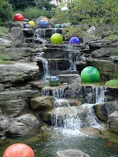 there are many balls floating on the water in this garden pond that is surrounded by rocks and boulders