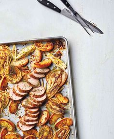 a pan filled with meat and vegetables on top of a white table next to utensils