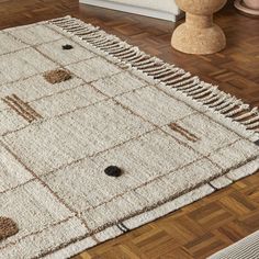 a white rug with brown squares and dots on the floor in front of a vase