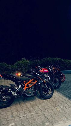 three motorcycles parked next to each other on a brick road at night with the lights on