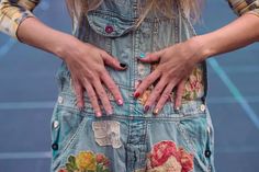 a woman with her hands on the back of her jean overalls that has flowers all over it