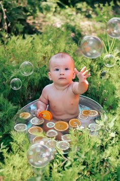 a baby sitting in the grass with soap bubbles around him and an orange on his chest