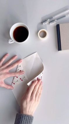 a person's hands on top of a box next to a cup of coffee