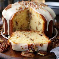 a bundt cake with white frosting and pecans around it on a wooden platter