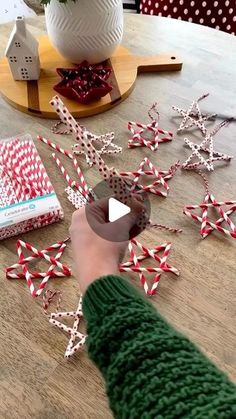 a person cutting up some paper stars on top of a wooden table with red and white striped straws