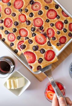 a person holding a spoon over a cake with strawberries and blueberries on it