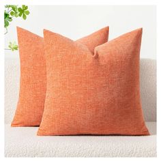 two orange pillows sitting on top of a white couch next to a potted plant