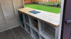 an outdoor kitchen with wooden counter tops and storage bins on the outside wall, next to a purple door