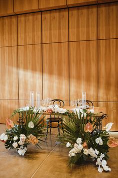 an arrangement of flowers and greenery on the floor in front of a wooden wall