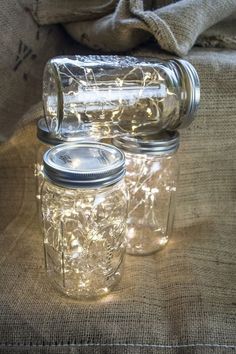 two mason jars with fairy lights in them sitting on a tablecloth covered couches